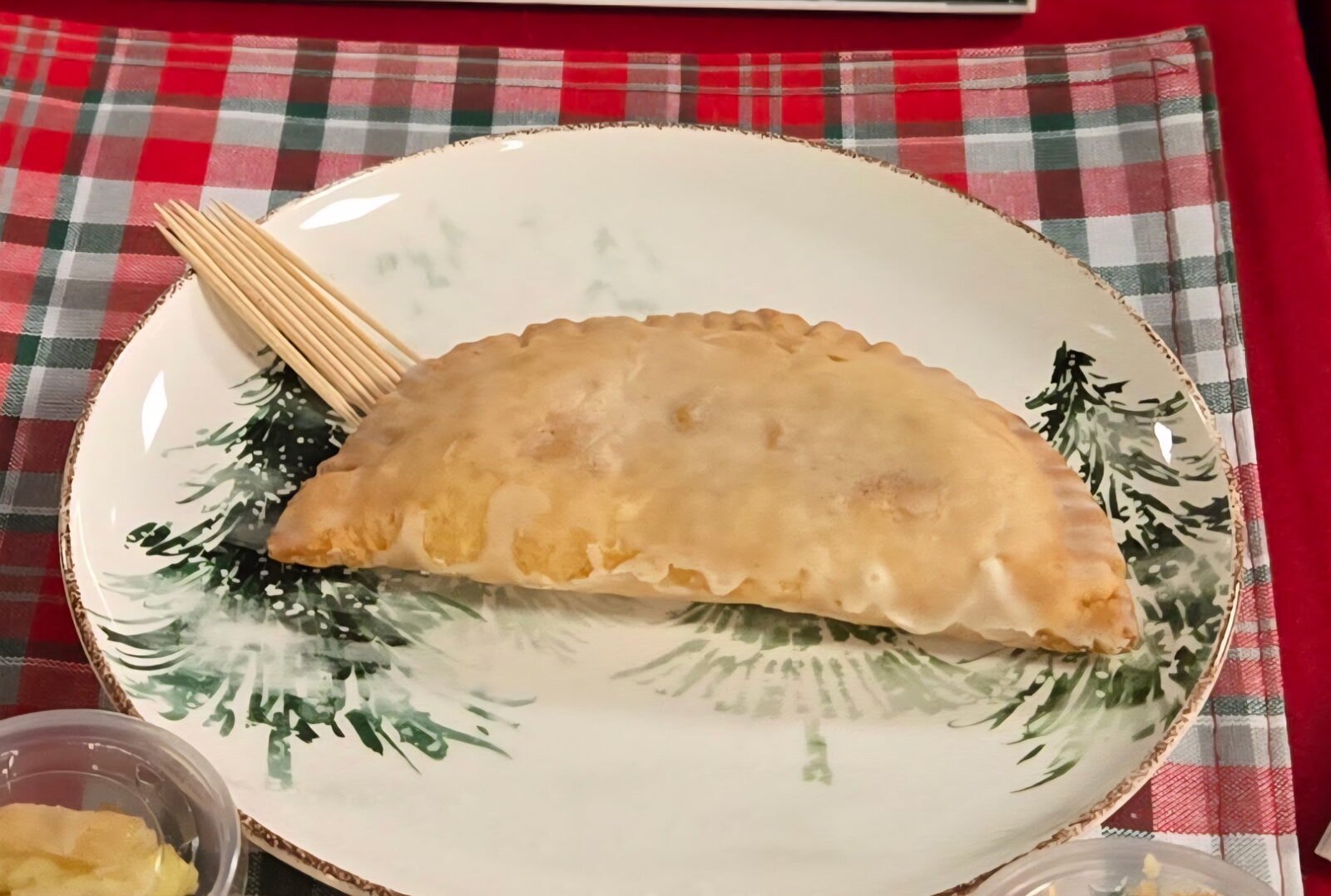 A fried pie served on a holiday plate with toothpicks, set out on a red plaid tablecloth