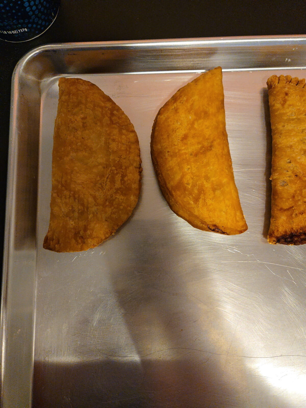Three deep-golden fried pies resting side by side on a metal sheet pan